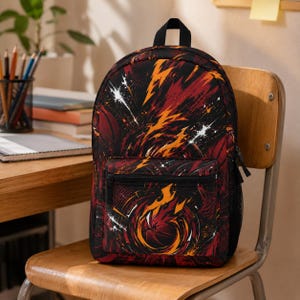 May include: A black backpack featuring a dynamic graphic print of basketballs surrounded by swirling orange and yellow flames, white lightning bolts, and dark red accents. The bag includes a top handle, a front zippered pocket, and side mesh pockets.