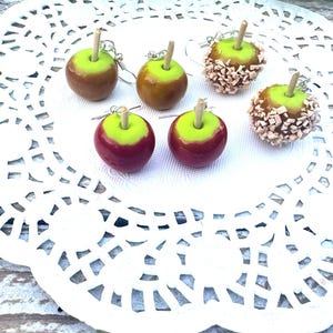 Op de afbeelding: Vier paar handgemaakte snoep-appel oorbellen. Twee paar zijn rood en groen, &eacute;&eacute;n paar is bruin en groen, en &eacute;&eacute;n paar is bruin en groen met witte sprinkles.