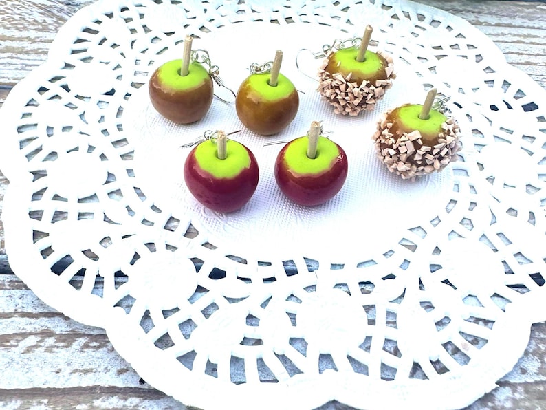 Op de afbeelding: Vier paar handgemaakte snoep-appel oorbellen. Twee paar zijn rood en groen, &eacute;&eacute;n paar is bruin en groen, en &eacute;&eacute;n paar is bruin en groen met witte sprinkles.