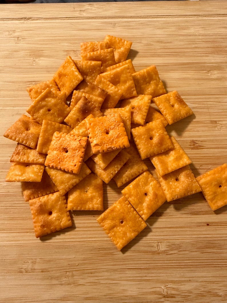 Puede incluir: Un mont&oacute;n de galletas cuadradas y anaranjadas, cada una con un agujero central. Est&aacute;n dispuestas sobre una tabla de madera marr&oacute;n claro. Las galletas tienen una superficie ligeramente texturizada.