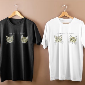 以下が含まれることがあります： 「show me your kitties」という文字と緑色の目をした2匹の猫のグラフィックが描かれたTシャツ2枚。左側のTシャツは黒色、右側のTシャツは白色です。