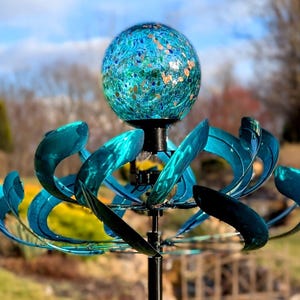 May include: A blue and green metal wind spinner with a glass globe on top. The globe has a blue and green speckled pattern with gold flecks. The wind spinner is on a black metal pole.