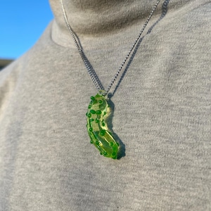 May include: A silver chain necklace with a green glass pickle pendant. The pickle has a bumpy texture and is translucent.