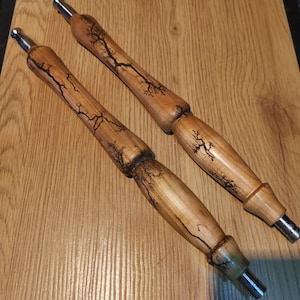Könnte beinhalten: Zwei Holz-Shisha-Schläuche mit dunkler Holzmaserung und schwarzen Blitzmustern. Die Schläuche haben an jedem Ende eine silberne Metallspitze.