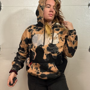 Puede incluir: Una sudadera con capucha de color marrón y negro con un logotipo de la NASA y el texto "NATIONAL AERONAUTICS AND SPACE ADMINISTRATION" en la parte delantera.