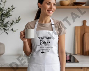 Peut inclure: Un tablier blanc avec le texte noir MADE WITH love means I licked the spoon & kept using it, accompagné d'une petite icône de cœur et d'un graphique de cuillère. Le tablier comprend une poche avant et est porté sur un t-shirt beige.