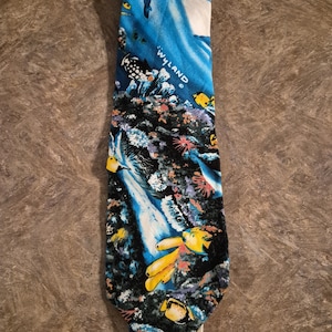 May include: A necktie with a vibrant underwater scene design. The tie features a blue background with white, yellow, and black marine life, coral, and the text "WYLAND". The tie is made of a smooth fabric.
