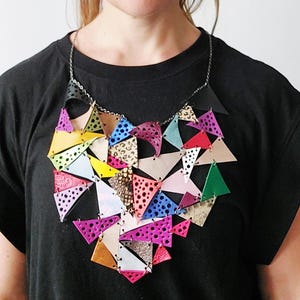 Può includere: Una collana di cuoio colorata composta da molti piccoli triangoli. La collana ha la forma di un cuore e presenta una varietà di colori, tra cui rosa, blu, verde, giallo e rosso.
