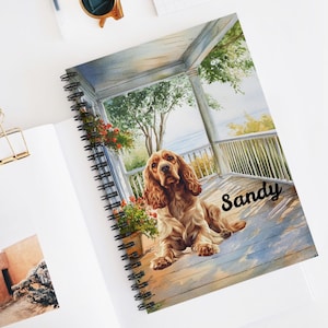 May include: A watercolor painting of a brown and white Cocker Spaniel dog sitting on a porch with the name "Sandy" written on the floor. The dog is looking to the right of the image. The porch has a white railing and a view of a body of water in the distance.
