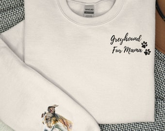 Peut inclure: Un sweat-shirt blanc avec le texte "Greyhound Fur Mama" et des empreintes de pattes sur le devant. La manche gauche présente une illustration aquarelle d'un lévrier avec le nom "Baxter" écrit en dessous.