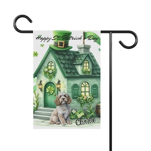 Puede incluir: Una bandera de jardín del Día de San Patricio con una casa verde con un sombrero de duende, tréboles y un perro llamado Charlie. La bandera está montada en un soporte de metal negro con una parte superior curva.