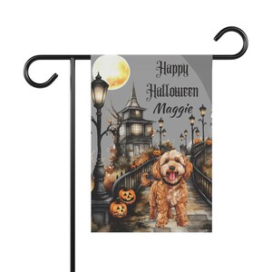 May include: A rectangular garden flag featuring a golden-brown dog standing on a stone bridge. The scene includes a haunted house, glowing street lamps, pumpkins, and a full moon. The text reads Happy Halloween Maggie in black gothic lettering.
