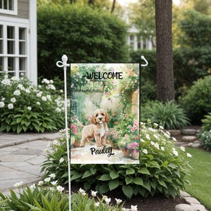 Puede incluir: Una bandera de jardín de bienvenida con una ilustración de acuarela de un perro marrón y blanco de pie en un jardín con flores rosas y enredaderas verdes. El texto "WELCOME" está en la parte superior de la bandera y el nombre "Pauley" está en la parte inferior.