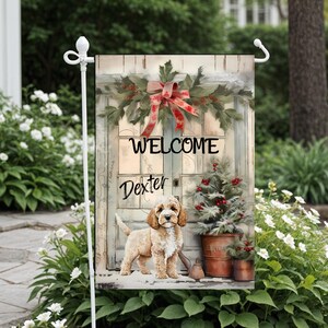 Puede incluir: Bandera de jardín decorativa con un perro Cockapoo frente a una puerta con el texto "WELCOME Dexter". La bandera presenta una escena navideña con una corona, un pequeño árbol de Navidad y un lazo rojo. Diseño festivo.