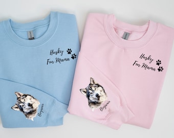 Op de afbeelding: Twee sweatshirts, één lichtblauw en één roze, elk met een husky-portret op de mouw en de tekst "Husky Fur Mama" met pootafdrukken. De mouw heeft ook de naam "Benjamin".