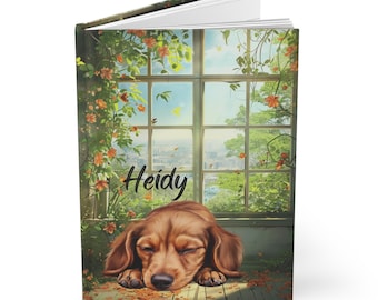 Könnte beinhalten: Ein Hardcover-Notizbuch mit einem schlafenden Dackel auf dem Cover. Der Hund ist braun mit geschlossenen Augen und liegt auf einem Holzboden. Der Hintergrund zeigt ein Fenster mit Stadtblick, umgeben von grünem Laub und dem Namen "Heidy".