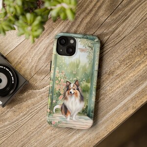 May include: A phone case with a watercolor illustration of a Sheltie dog standing in a garden with flowers and a butterfly. The dog is brown, white, and black with a pink nose and tongue. The background is a green garden with a blue door.