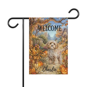 May include: A rectangular garden flag hanging on a black metal stand. The flag features a light-colored puppy standing on a path surrounded by orange pumpkins, autumn flowers, and a tree. The text WELCOME is at the top and Charlie is at the bottom.