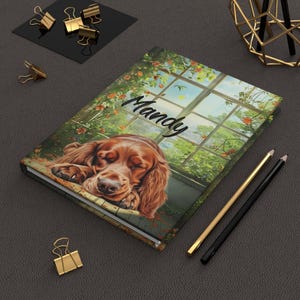 May include: A personalised journal featuring a brown dog sleeping in a window with green vines and the name "Mandy" written on the cover.