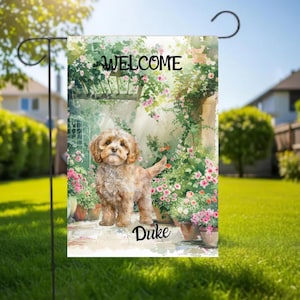 May include: A garden flag with a watercolour illustration of a dog named Duke, set against a floral backdrop. The flag displays the word "WELCOME" at the top. The dog is light brown with curly fur. Potted flowers surround the dog.