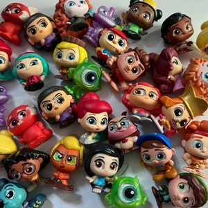 May include: A collection of 25 small, colorful, plastic figurines of Disney characters. The characters include Ariel, Belle, Mulan, Moana, Tiana, Rapunzel, and more. The figurines are all in a cartoon style with large eyes and bright colors.