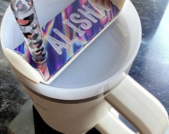 May include: A white travel mug with a lid and a handle. The lid has a slot for a straw and a personalized name tag that says "ALISHA" in silver lettering on a holographic background.