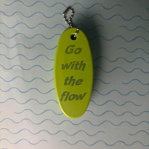 May include: A green oval keyring with a silver chain. The keyring has the text "Go with the flow" engraved on it.