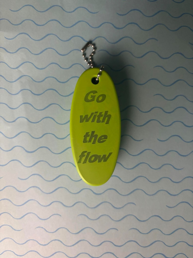 May include: A green oval keyring with a silver chain. The keyring has the text "Go with the flow" engraved on it.