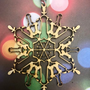 May include: A wooden snowflake ornament with a unique design. The snowflake is made of a light brown wood and has a intricate pattern.