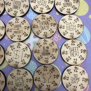 May include: Wooden tokens with bunny illustrations and various phrases, including "Choose Dinner", "Day with Dad", "Friend Sleepover", "Choose a Project", "Extra Snack", "Day with Mum", "£1", "30 Min Extra Screen Time", "Sweet Treat", "Game Night", "£2", and "No Chore Day".