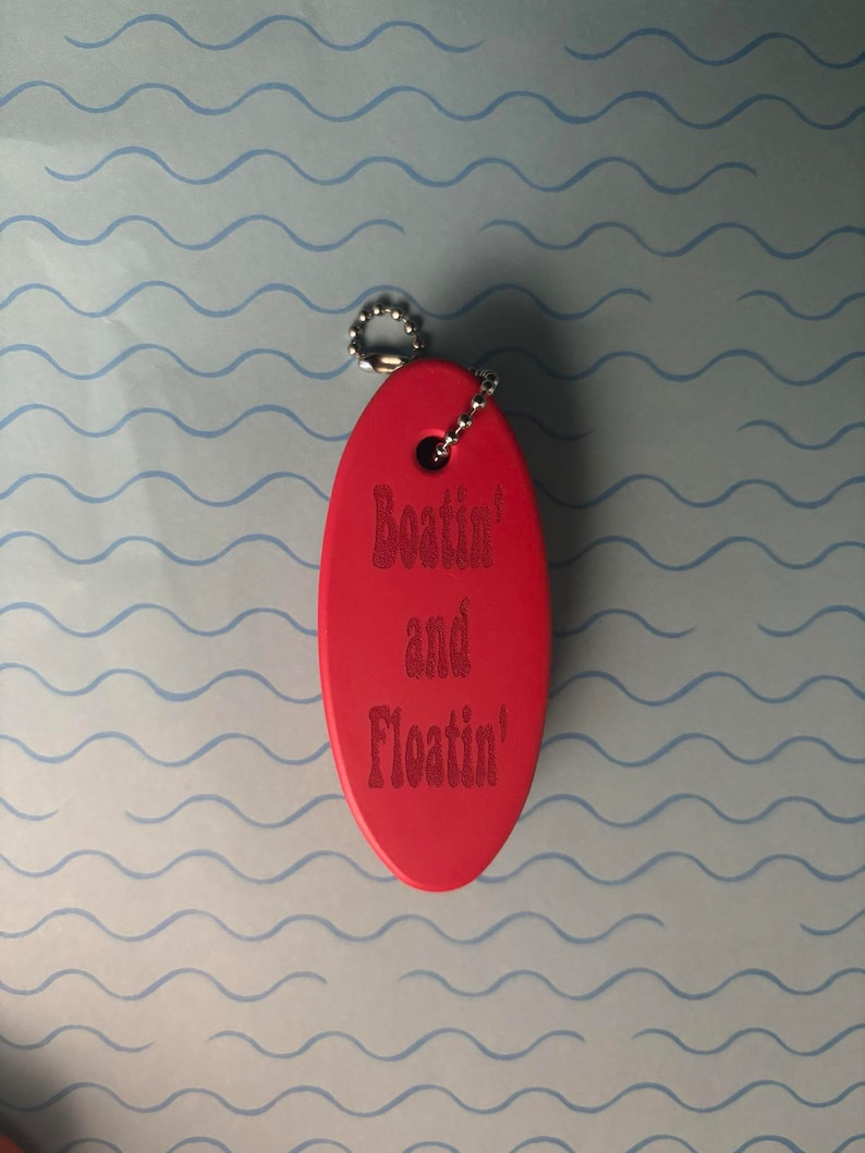May include: Red oval-shaped keyring with a silver chain. The keyring has the text "Boat'n and Float'n" engraved on it.