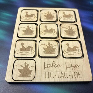 May include: A wooden tic-tac-toe game with a lake life theme. The game board has nine squares, each with a different image of people in a boat. The game board is made of light wood and has the words "Lake Life Tic-Tac-Toe" printed on it.