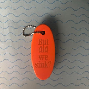 May include: Orange oval-shaped keyring with a silver chain and the text "But did we sink?"
