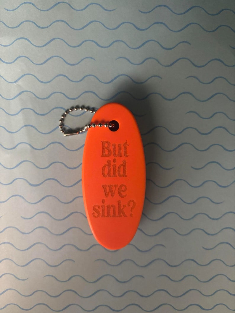 May include: Orange oval-shaped keyring with a silver chain and the text "But did we sink?"