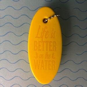 May include: Yellow oval-shaped keyring with a silver chain. The keyring has the text "Life is Better on the Water" printed on it.