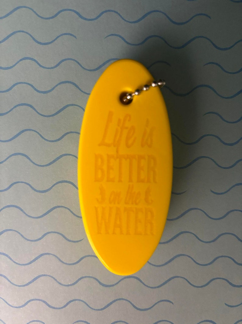 May include: Yellow oval-shaped keyring with a silver chain. The keyring has the text "Life is Better on the Water" printed on it.