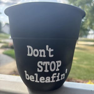 Puede incluir: Maceta de plástico negra con texto blanco que dice "Don't STOP beleafin'"