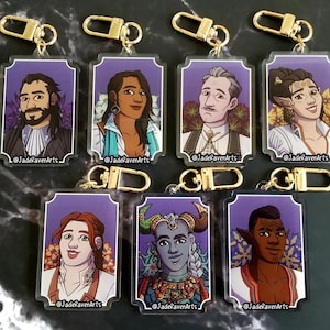 May include: A selection of character art keyrings with gold-coloured fixings. Each keyring displays a different character portrait against a purple backdrop with floral details. The artist's name, "JadeRavenArts", is printed on each keyring.