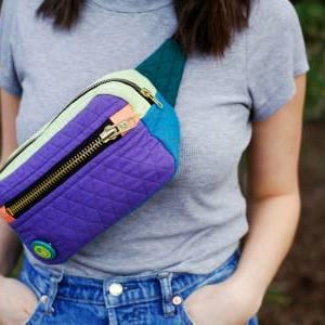 K&ouml;nnte beinhalten: Eine mehrfarbige gesteppte Bauchtasche mit Rei&szlig;verschluss und einem kleinen runden Knopf. Die Bauchtasche besteht aus verschiedenen Stoffen, darunter Lila, Blau, Gr&uuml;n und Gelb.