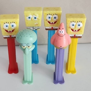 May include: Six colorful character-themed candy dispensers. The dispensers are shaped like a yellow sponge, a pink starfish, a green octopus, and three yellow sponges with different facial expressions.