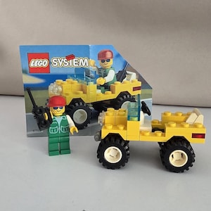 May include: A yellow Lego System jeep with black wheels and a white roll bar. A Lego figure in a green vest and red helmet stands next to the jeep. The box art shows a similar jeep and figure.