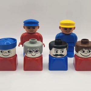 Op de afbeelding: Set van zes vintage plastic speelgoedpoppetjes met verschillende kapsels en gezichtskenmerken. De poppetjes dragen hoeden en hebben verschillende gekleurde lichamen. De poppetjes lachen allemaal.