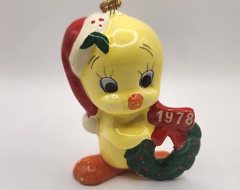 Può includere: Ciondolo natalizio in ceramica gialla a forma di uccello con un cappello di Babbo Natale e che tiene una ghirlanda verde con un nastro rosso su cui è scritto "1978".