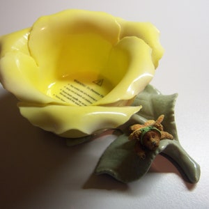 Peut inclure: Une rose en céramique jaune avec une petite figurine d'ours brun assise sur une feuille verte. La rose est un bougeoir avec une étiquette d'avertissement à l'intérieur.