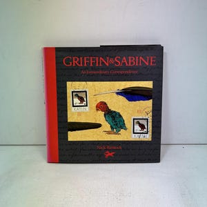 May include: A hardcover book titled "Griffin & Sabine: An Extraordinary Correspondence" by Nick Bantock. The cover is black with red accents and features illustrations of a bird, stamps, and a feather.