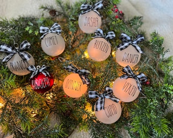 May include: Nine white Christmas ornaments with black and white checkered ribbon bows. Each ornament has a different reindeer name written on it: Prancer, Comet, Donner, Vixen, Dasher, Blitzen, Dancer, Cupid, and Rudolph. One ornament is red.