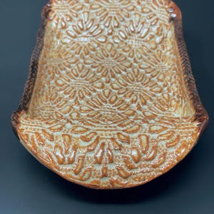 May include: A white ceramic serving dish with a brown glaze and a raised, intricate pattern. The dish has a rectangular shape with rounded edges.