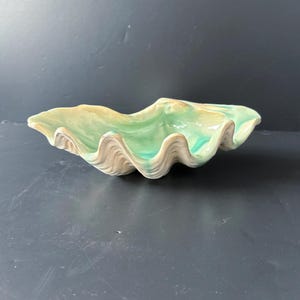 May include: A ceramic clam shell dish with a green and white glaze. The dish is shaped like a clam shell and has a smooth, glossy finish.