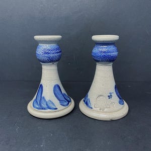 May include: A pair of blue and white ceramic candle holders with a stylized leaf design. The holders are marked with the words "ANDOR" and a logo.