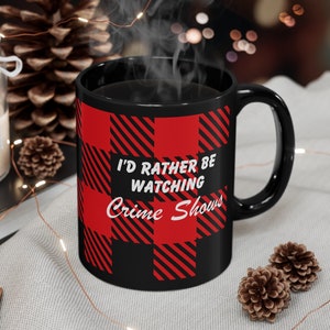May include: Black coffee mug with a red and black buffalo plaid pattern. The mug has white text that reads "I'd rather be watching Crime Shows".